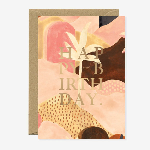 A birthday greeting card with abstract floral patterns and 'HAPPY BIRTHDAY' text in gold foil on the front. It is accompanied by a brown envelope.