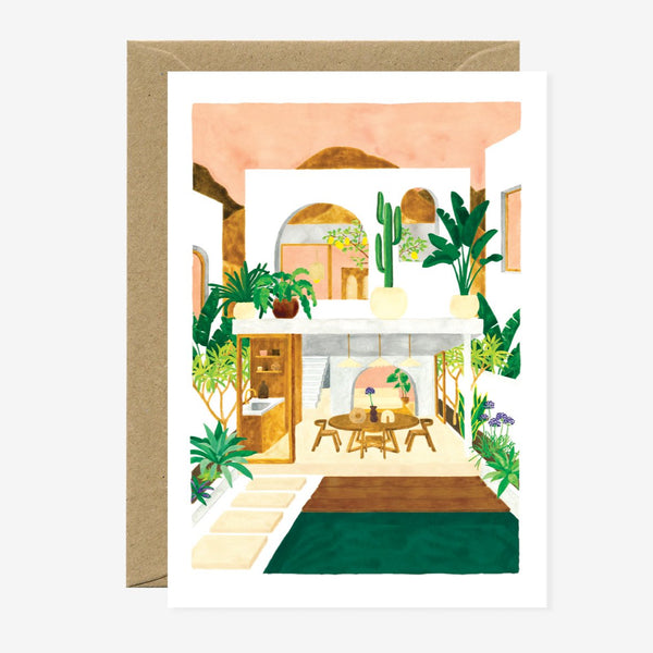 A greeting card featuring an illustration of an interior space with plants and a wooden table, accompanied by a brown envelope.