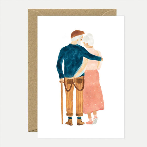 Illustration of an elderly couple embracing. The man is wearing a blue sweater and a hat, and the woman is wearing a pink skirt and blouse.
