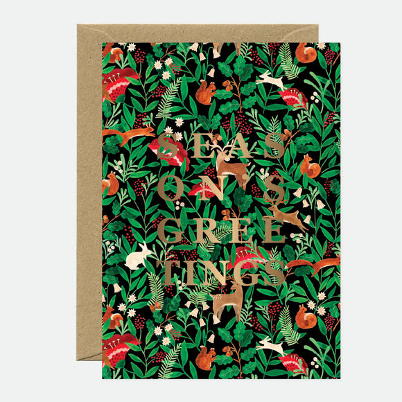 A Christmas greeting card with a gold foil detailed pattern of animals and the text 'Merry Christmas' on it, accompanied by a brown envelope.