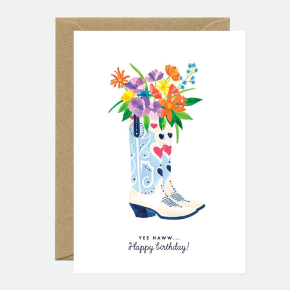 A birthday greeting card with a floral design in a boot, with a 'Happy Birthday' text, presented with a brown envelope.