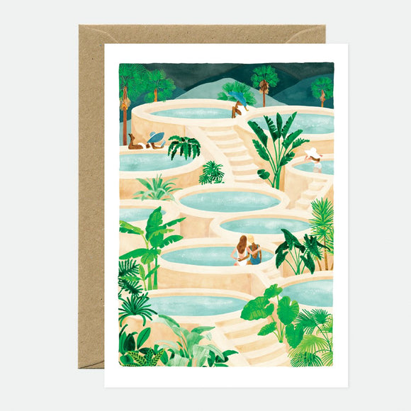 A greeting card depicting a tropical landscape with lush greenery and water features, accompanied by a brown envelope.