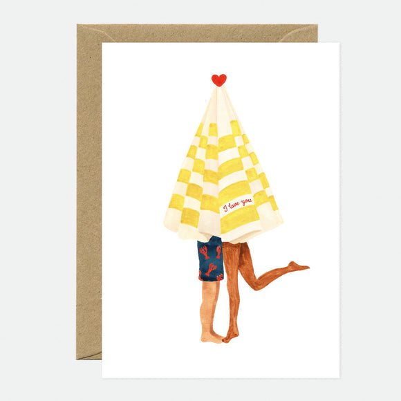 A greeting card with an illustration of a beach umbrella with a 'I love you' text on it, shared by two stick figure characters. The card is accompanied by a brown envelope.