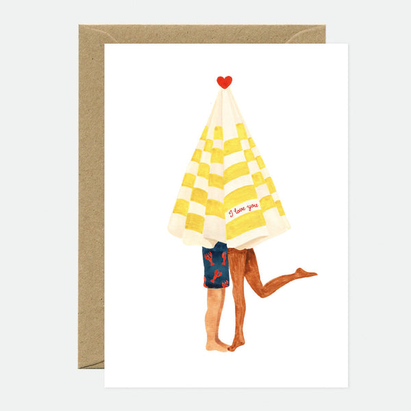 A greeting card with an illustration of a beach umbrella with a 'I love you' text on it, shared by two stick figure characters. The card is accompanied by a brown envelope.