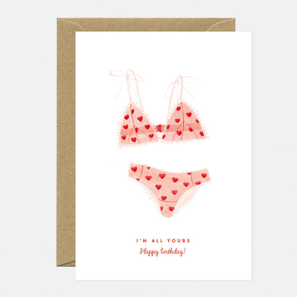 Greeting card with illustration of a pink bikini with red hearts, and text 'I'm all yours! Happy Birthday!'