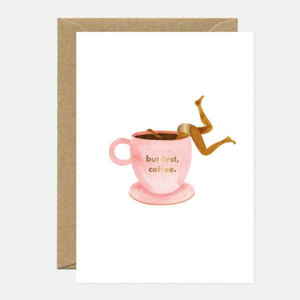 A greeting card with an illustration of a coffee cup and a gold foil detail. The text on the cup reads 'but first, coffee.