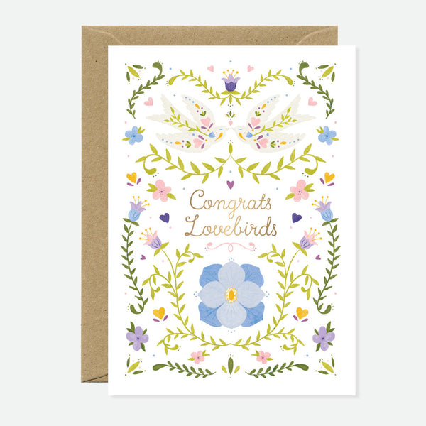 A greeting card with floral patterns and the text 'Congrats Lovebirds' adorned with gold foil details. A brown envelope accompanies the card.