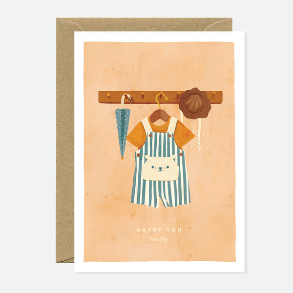 Greeting card with an illustration of a cartoon bear wearing a striped apron and hanging items on a wooden rail, with a recycled brown envelope.