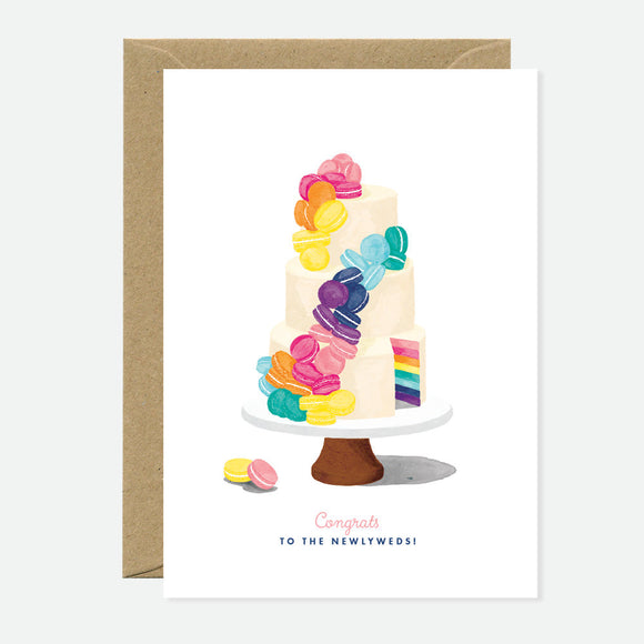 A greeting card with an illustration of a colorful, multi-tiered cake on a stand, with a accompanying brown envelope. The text on the card reads 'Congratulations to the newlyweds!'.