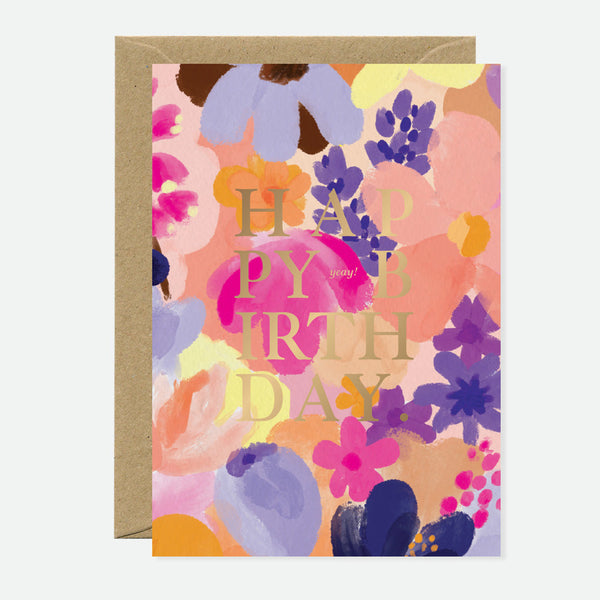 A vibrant floral greeting card with gold foil text that reads 'Happy Birthday' on a pink, purple, and orange floral background, accompanied by a brown envelope.