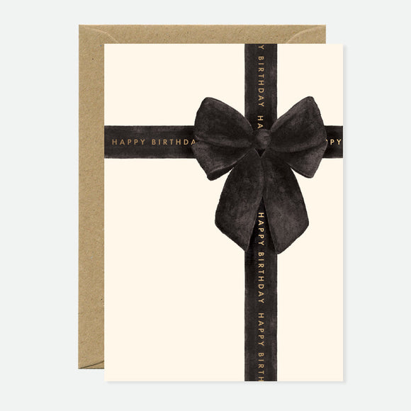 A greeting card with a black bow and 'Happy Birthday' text on it, accompanied by a brown envelope.