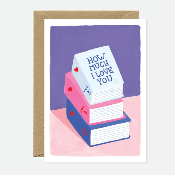 A greeting card with an illustration of three books in pink, blue, and white colors with the phrase 'HOW MUCH I LOVE YOU' written on the top book. The card is placed against a purple background, and a brown envelope accompanies it.