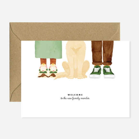 Greeting card featuring a dog sitting between two people’s legs, symbolizing the arrival of a new family pet and the joy of companionship.