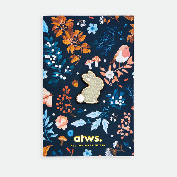Baby Rabbit enamel pin by All the Ways to Say featuring gold-plated bunny with glitter finish on illustrated floral forest background with mushrooms and birds.