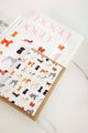 Birthday card illustrated with colorful dogs and gold foil “Happy Birthday” text, placed on a kraft envelope.