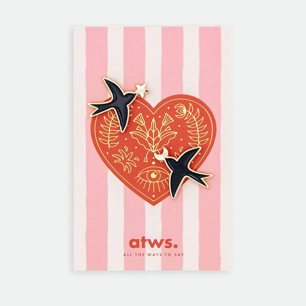 Swallows Duo enamel pin by All the Ways to Say featuring two gold-plated black swallows on pink striped background with red heart and golden motifs.