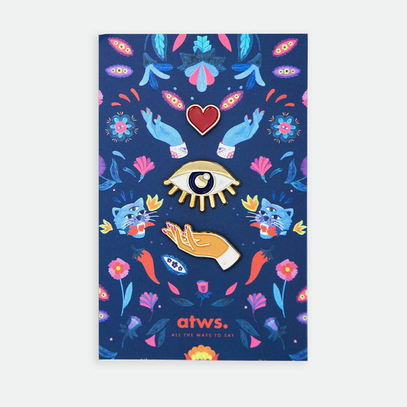 Heart on Hand XL enamel pin by All the Ways to Say featuring gold-plated hand, eye and heart design on vibrant blue floral mystical background.