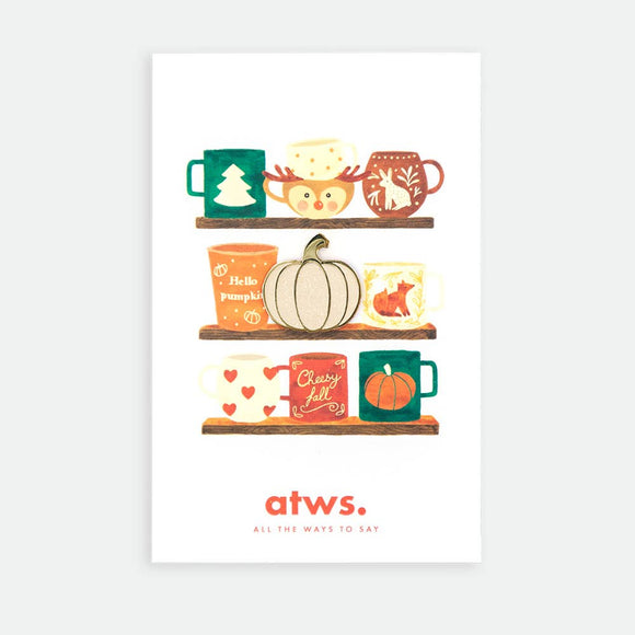 Pumpkin enamel pin by All the Ways to Say featuring gold-plated pumpkin design on illustrated mug shelf background with warm fall tones.