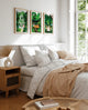 Set of three Namaster tropical art prints framed above a bed with neutral bedding and soft light