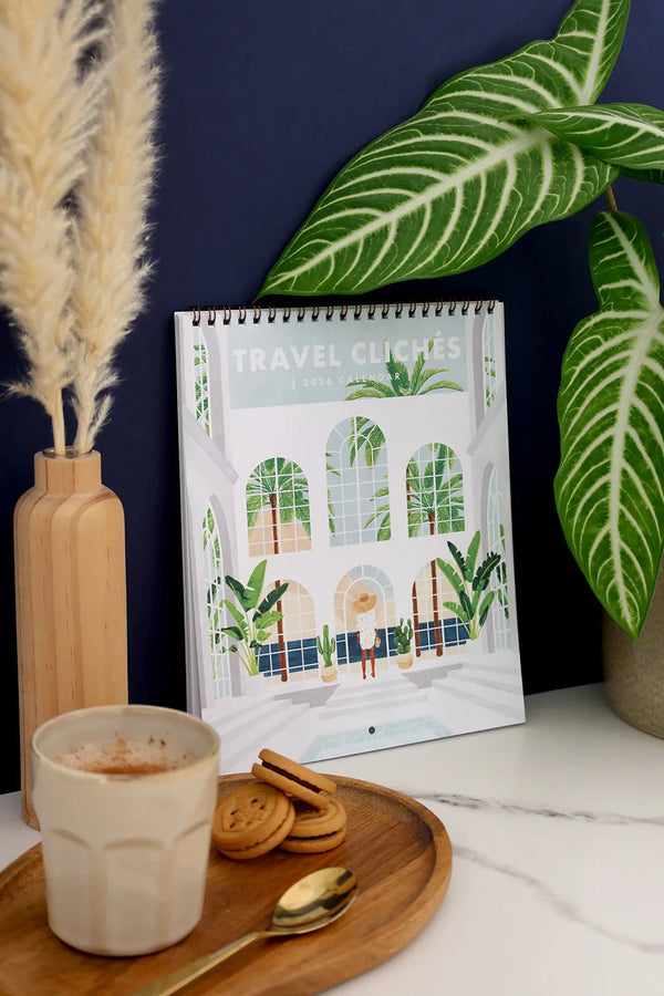 Close-up of Travel Clichés 2026 calendar cover – woman standing in tropical glasshouse illustration