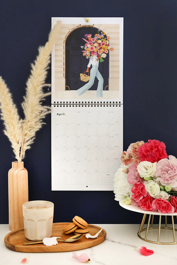 April page of Travel Clichés 2026 calendar – woman carrying large bouquet of flowers in Paris street