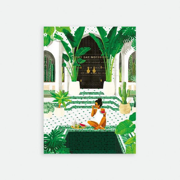 A5 sized notebook with a gold foil cover featuring an illustration of a woman sitting in a lush garden setting with archways and plants.