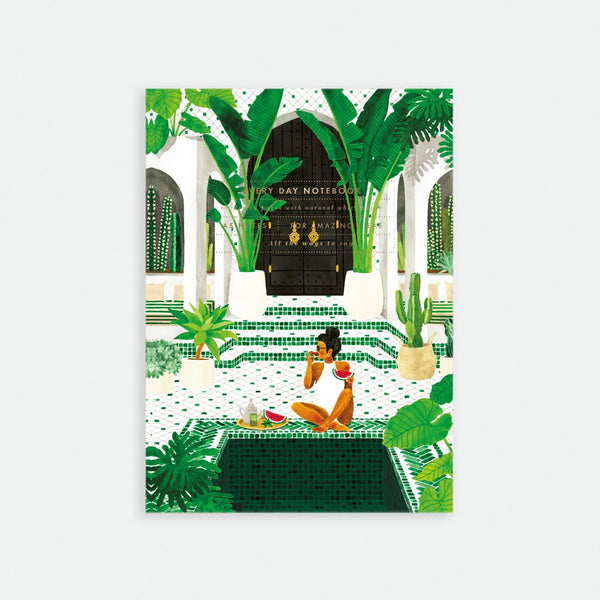A5 sized notebook with a gold foil cover featuring an illustration of a woman sitting in a lush garden setting with archways and plants.