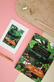 Yoga retreat illustrated notebook styled with gold pen, clips, and postcard on pink background for creative stationery flatlay.