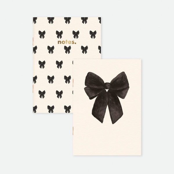 Set of two A6 pocket notebooks, one with large black bow illustration, the other with repeated bow pattern and gold “notes” detail, by All the Ways to Say.