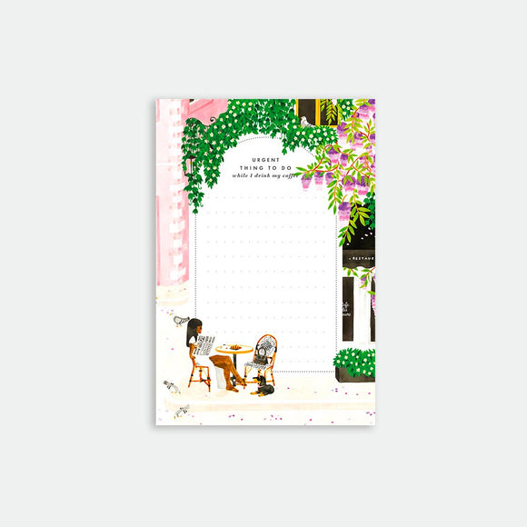 A colorful notepad with an illustration of a street scene in Paris, featuring a cafe and a woman sitting at a table.