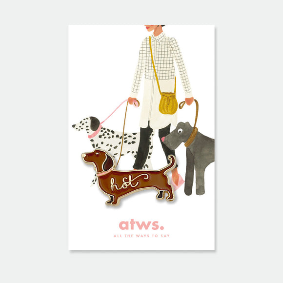Hot Dog enamel pin by All the Ways to Say featuring brown dachshund with gold-plated finish and “hot” script on illustrated dog-walking background.