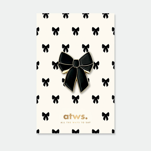 Black Bow enamel pin by All the Ways to Say featuring glossy black ribbon design with gold-plated finish on cream background with bow pattern.