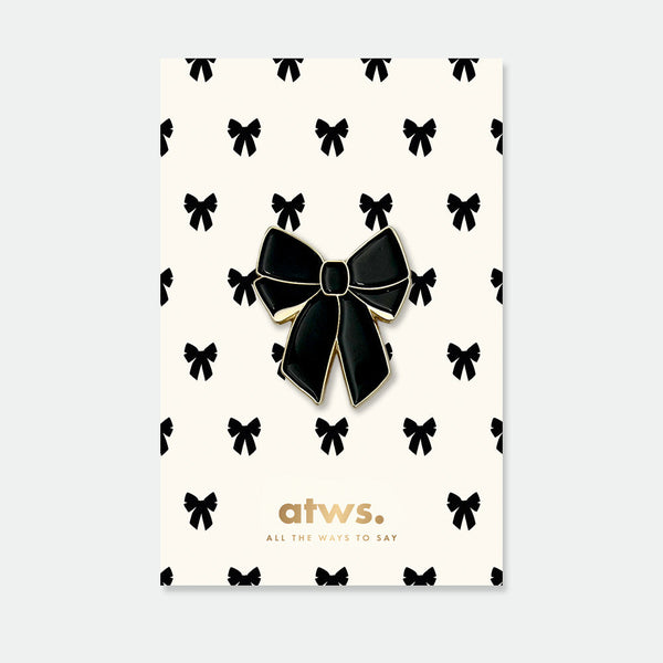 Black Bow enamel pin by All the Ways to Say featuring glossy black ribbon design with gold-plated finish on cream background with bow pattern.