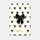 Black Bow enamel pin by All the Ways to Say featuring glossy black ribbon design with gold-plated finish on cream background with bow pattern.
