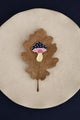 Crazy Mushroom enamel pin by All The Ways To Say on oak leaf over beige plate – navy blue background, minimal fall style