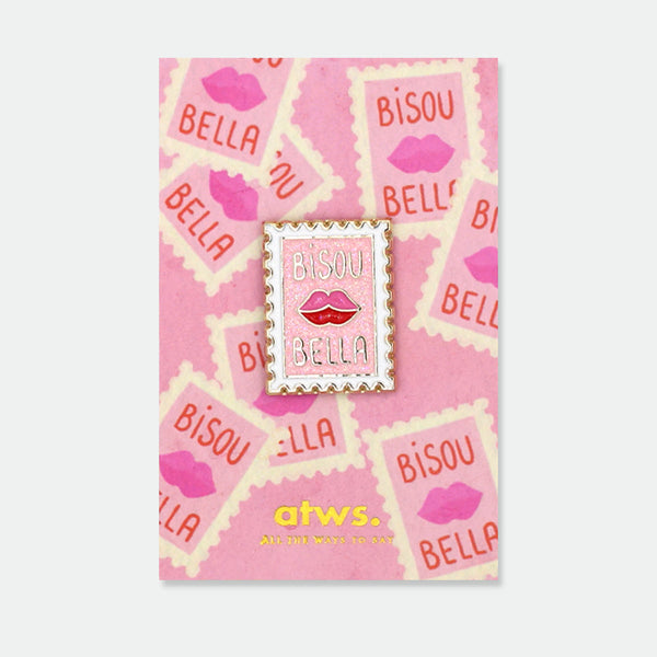 Bisou Bella enamel pin by All the Ways to Say featuring pink and gold postage stamp design with red lips and glitter details on pink kiss background.