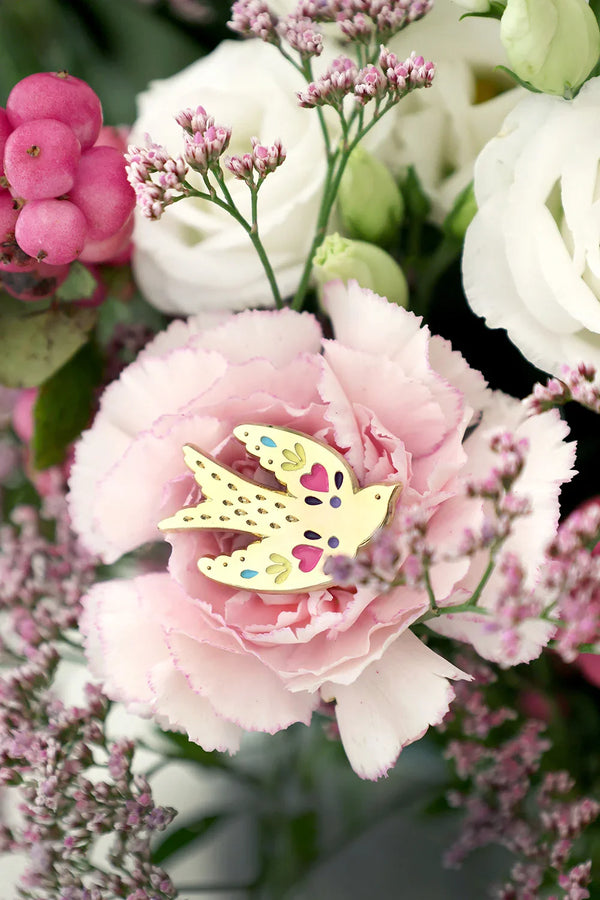 Detailed view of Lovebird enamel pin by All The Ways To Say – colorful bird on soft pink flower petals