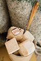 Macro view of Santa’s Cup enamel pin by All The Ways To Say – red striped mug and glitter details on marshmallow background