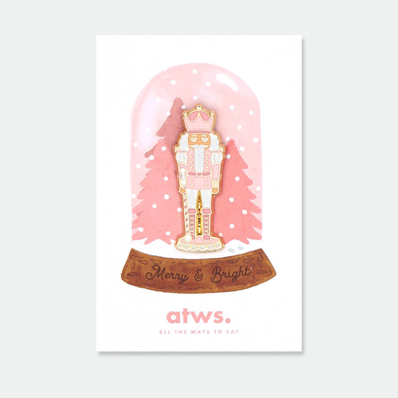 Pink Nutcracker enamel pin by All the Ways to Say featuring pink and gold nutcracker design with festive details, displayed on Merry & Bright holiday card.