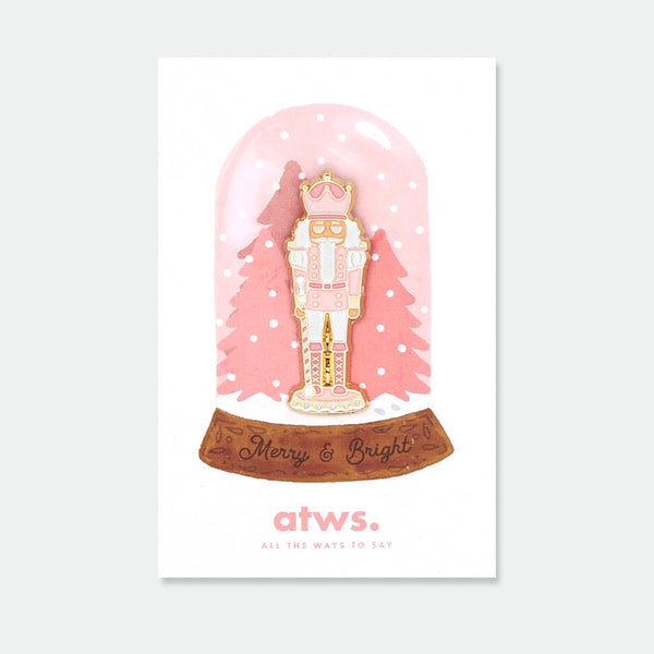 Pink Nutcracker enamel pin by All the Ways to Say featuring pink and gold nutcracker design with festive details, displayed on Merry & Bright holiday card.