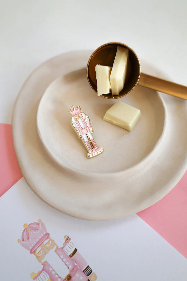 Close-up of Pink Nutcracker enamel pin by All The Ways To Say – candy-inspired design with gold and pink tones on ceramic plate