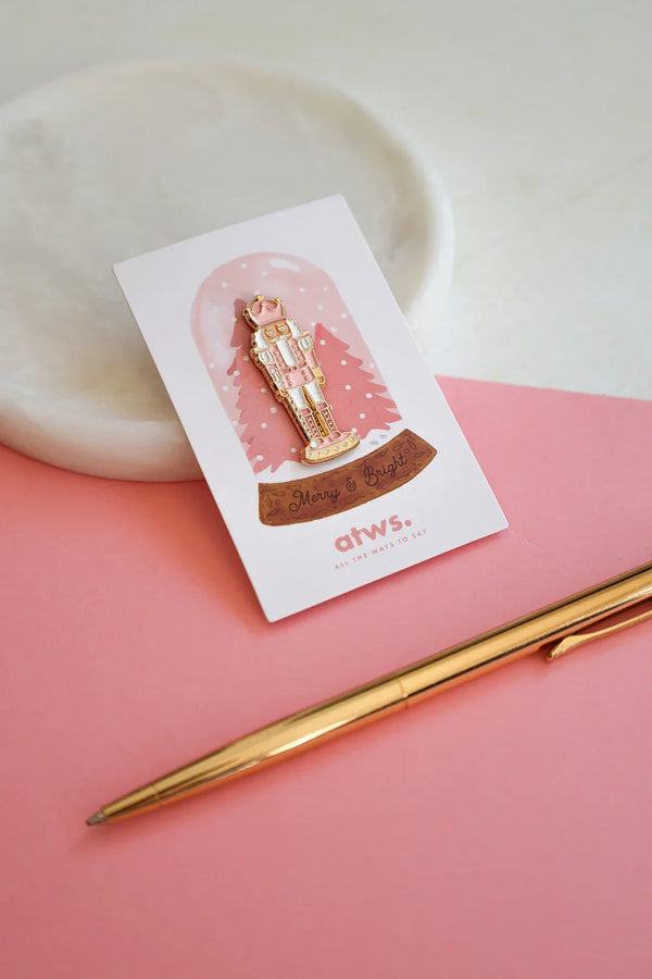 Pink Nutcracker enamel pin by All The Ways To Say on gift card – Christmas nutcracker design with pink trees and gold details