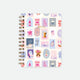 A spiral notebook with a colorful cover featuring various designs and text elements, such as 'BISOUS' and 'BISOU BISOU' in a grid pattern.