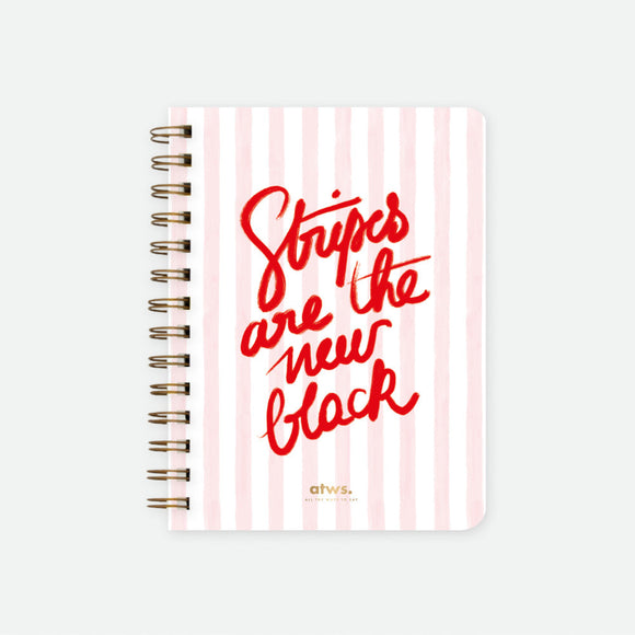 A spiral notebook with a pink striped cover and the text 'Stripes are the new black' written in a red, cursive font.