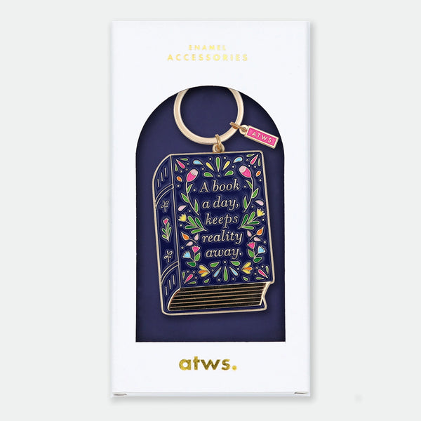 Enamel and metal keychain shaped like a navy storybook covered in colorful flowers, text reading "A book a day, keeps reality away," gold-tone ring and "ATWS" charm