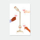 A gold enamel pin set featuring a rose wine bottle pouring into a glass connected by a chain, displayed on an illustration of hands toasting.