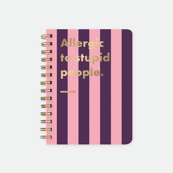 Allergic To Stupid People A5 spiral notebook by All The Ways To Say, bold purple and pink striped cover with "Allergic to stupid people." text in gold foil lettering and a gold underline, spiral binding visible on the left edge