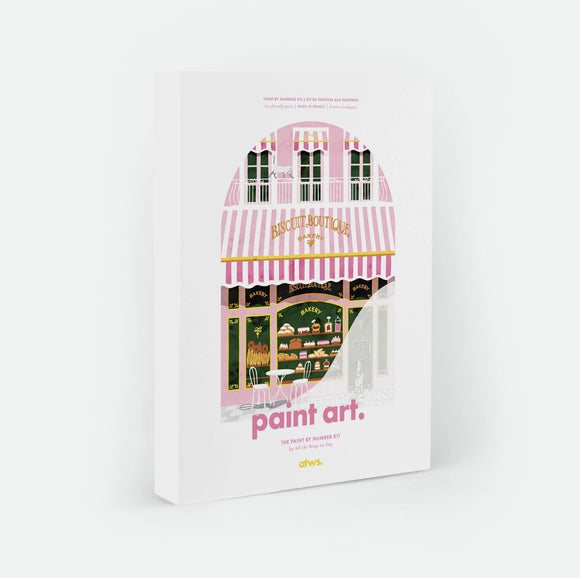 Bakery paint by numbers kit box by All The Ways To Say, illustration of a pink and white striped "Biscuit Boutique" bakery storefront with pastries in the window, a white cat on the balcony above and a Dalmatian outside on the pavement, "paint art. The Paint By Number Kit by All The Ways To Say"