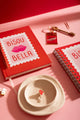 Bisou Bella - Notebook A5: a full collection display including the A5 notebook, a spiral planner, and a chocolate bar keychain.