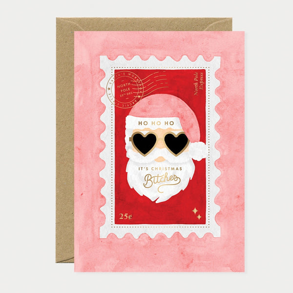 Illustrated Christmas card designed as a postage stamp featuring Santa Claus wearing heart-shaped sunglasses, gold foil postmark reading "North Pole, 25th Dec" and "North Pole Express," text reading "Ho Ho Ho, It's Christmas Bitches" with "Bitches" in gold foil script, and a "25¢" stamp value in the corner